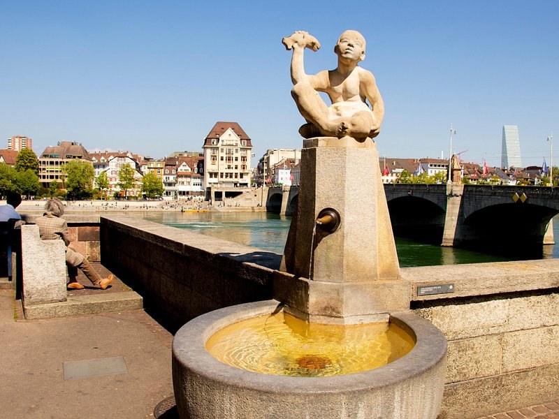 A bronze fountain figure by the river, a stone bridge behind it