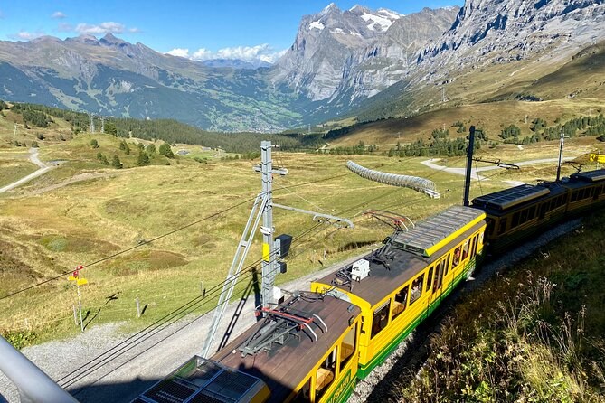A yellow mountain train climbing through high pasture below the peaks